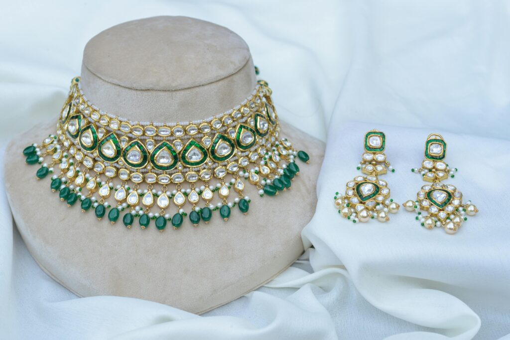 Luxurious gold and green jewelry set featuring intricate beadwork and pearls displayed on a fabric backdrop.