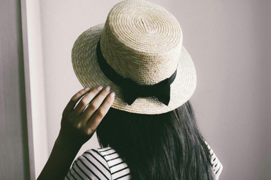 Woman wearing a straw hat with a black ribbon, posing indoors. Fashionable and modern look.