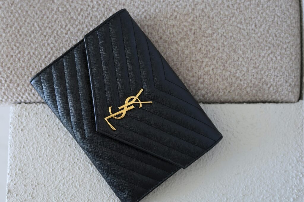 Elegant black leather clutch with a prominent gold accent on textured background.